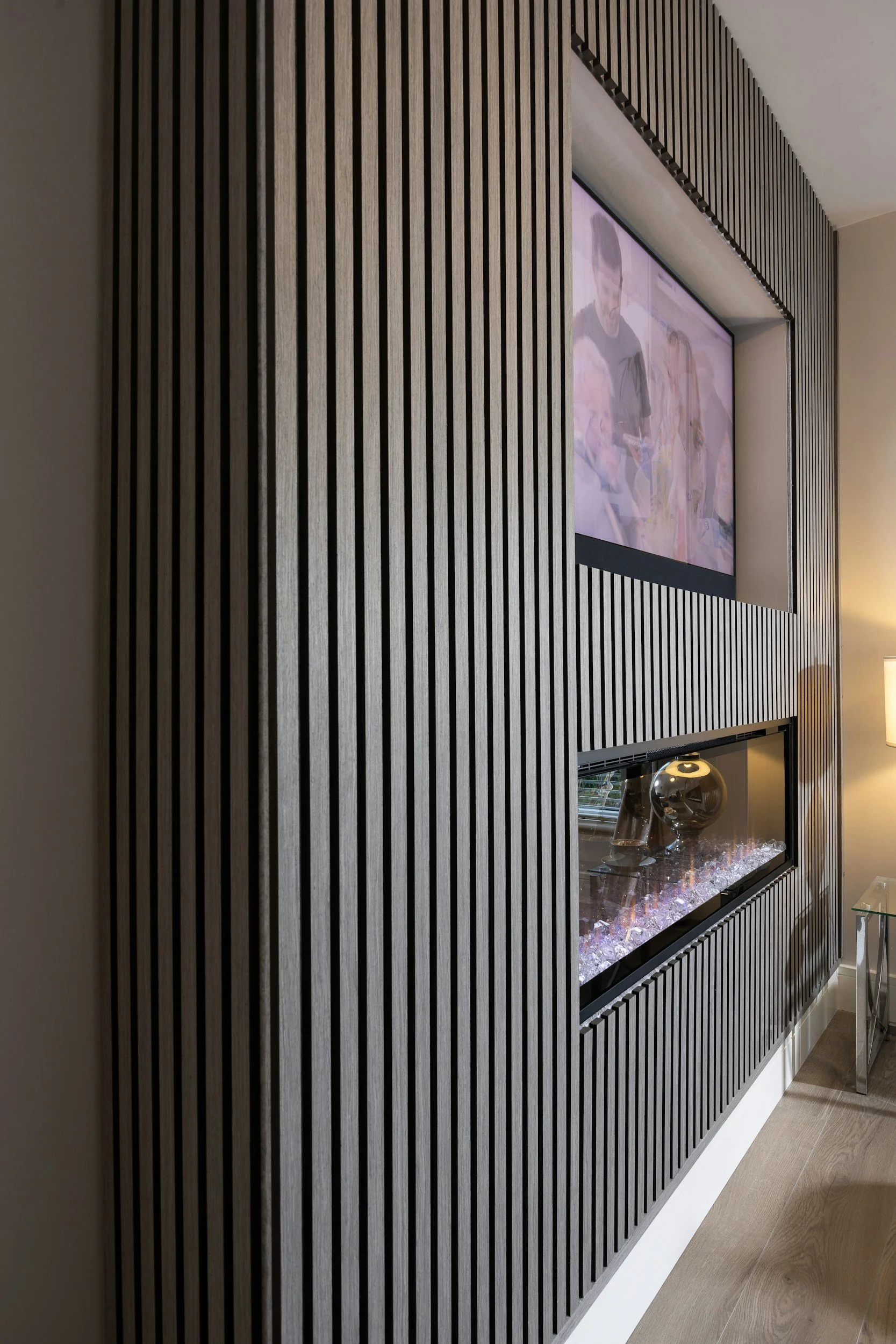 Interior of a room with a built-in fireplace and a mounted flat-screen TV, surrounded by vertical wooden slats on the wall.