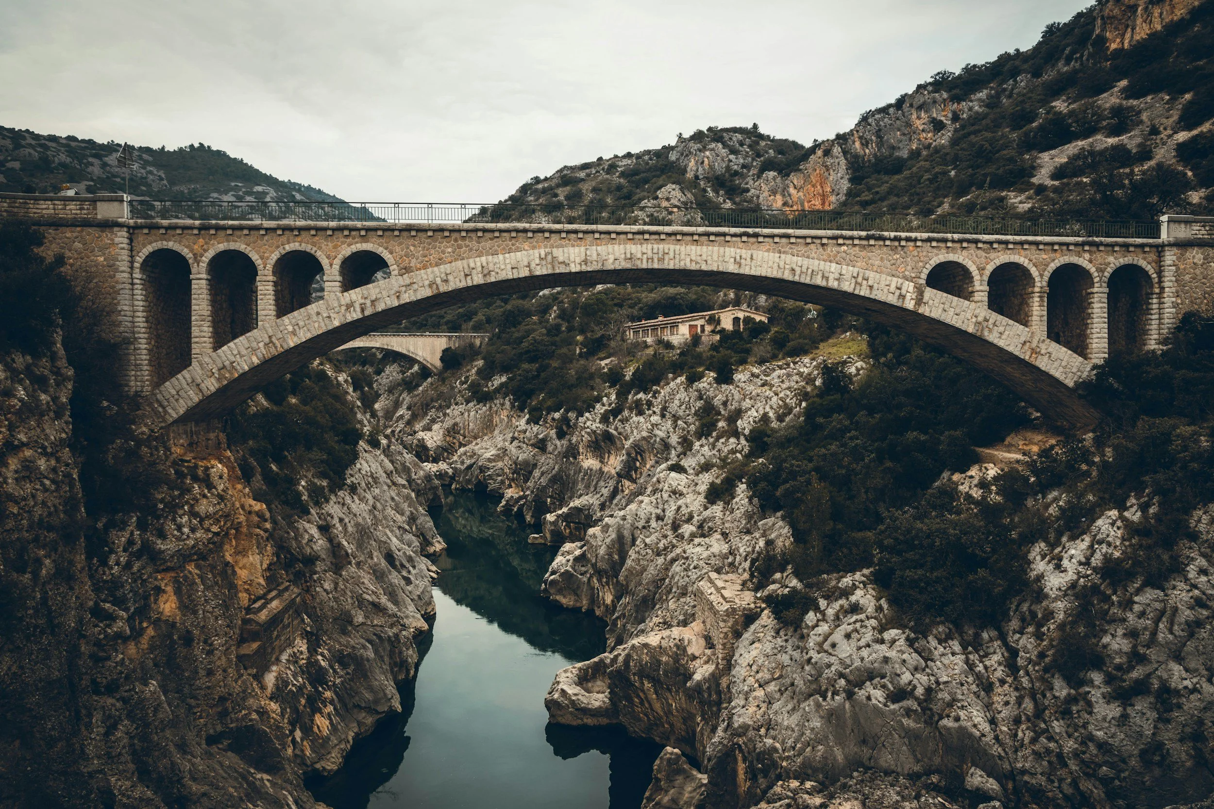 A stone arch bridge spanning over a rocky canyon with a narrow waterway at the bottom, surrounded by rugged hills and sparse vegetation.