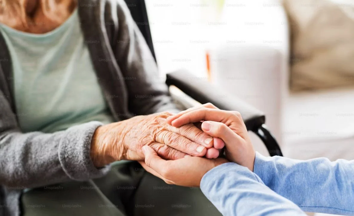 A young person holding the hand of an elderly woman in a care facility.