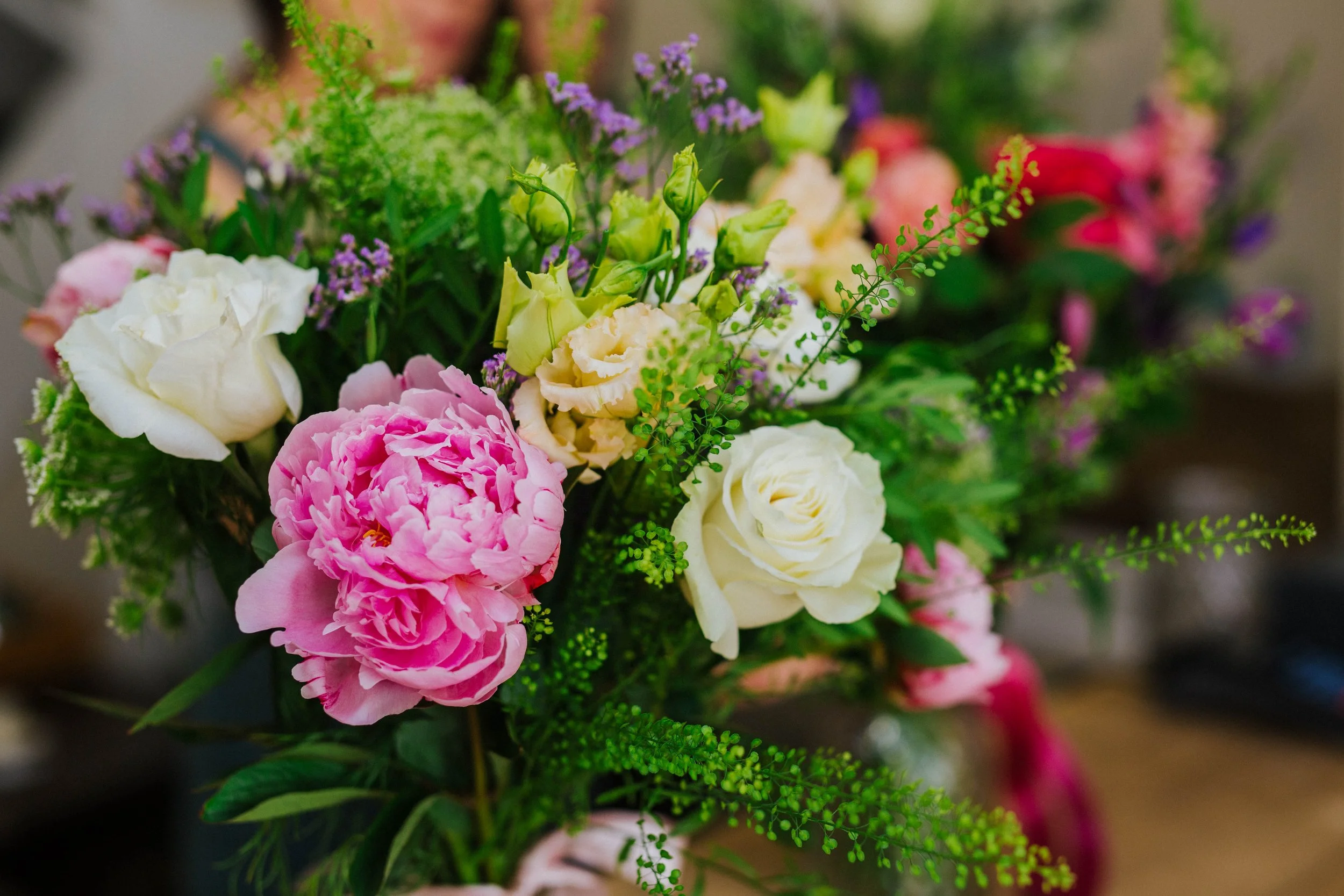 A colorful bouquet of various flowers including pink peonies, white roses, purple statice, and green foliage.