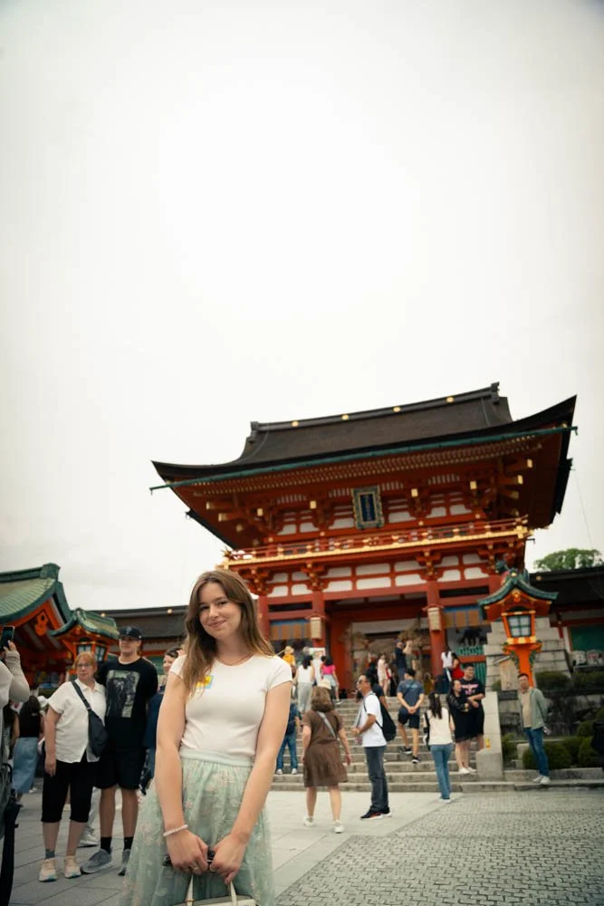 A young woman stands in front of a traditional Japanese temple with a large crowd of tourists around her.