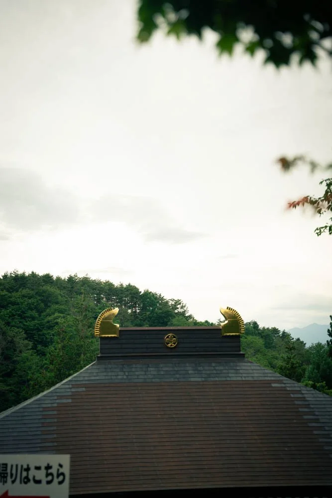 Roof of a building with two decorative golden mythical creature ornaments and a circular emblem in the center, set against a background of green trees and a cloudy sky.