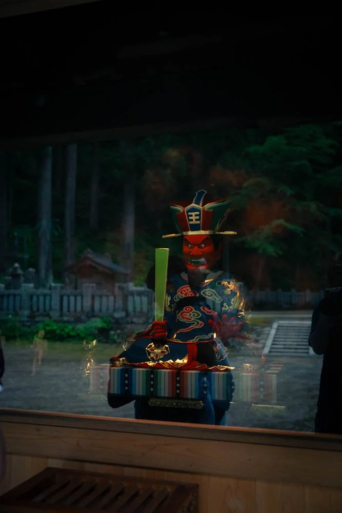 Colorful Japanese ninja or samurai statue with a hat, holding a sword, and wearing traditional clothing, displayed outdoors with a forest background.