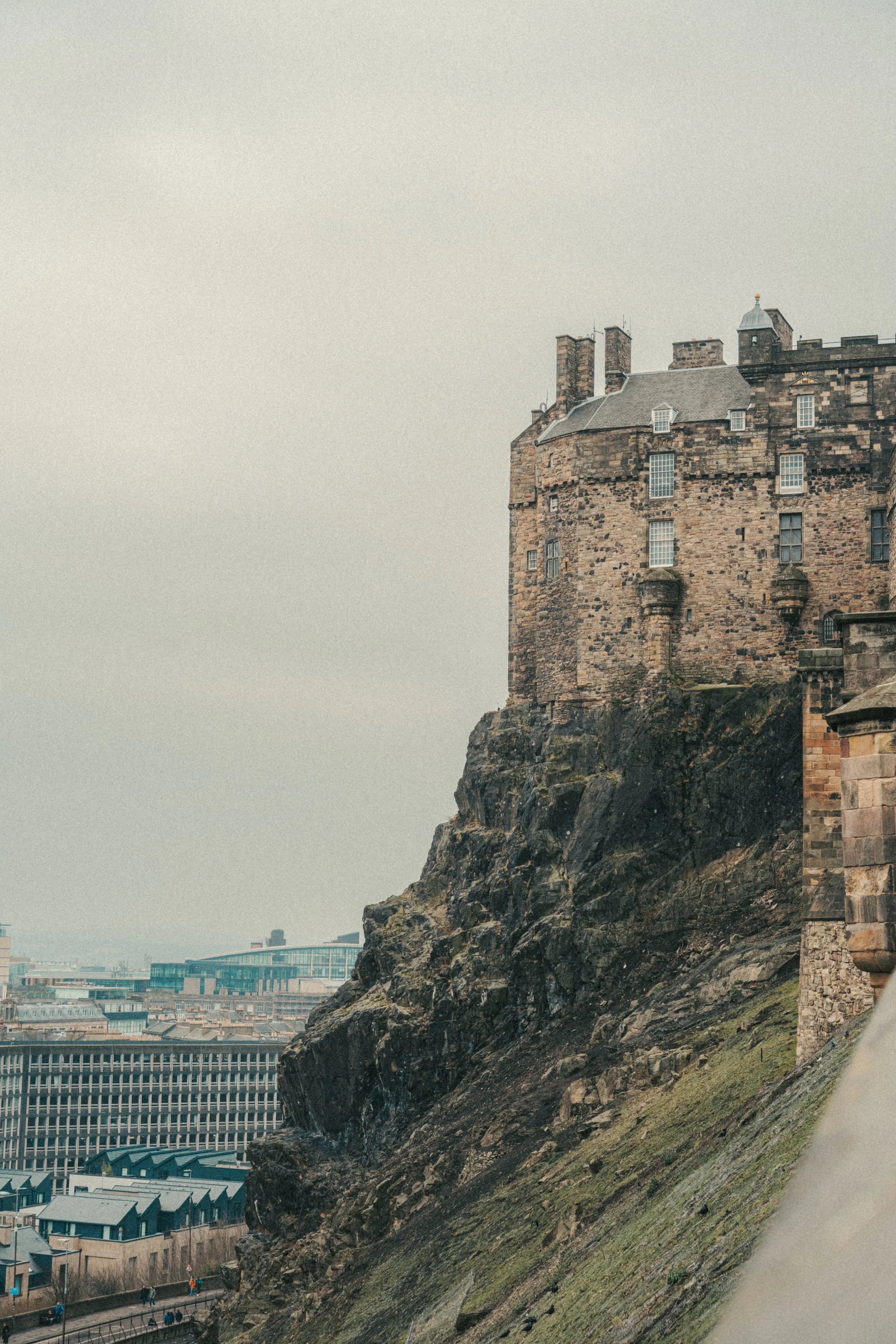 A large historic castle is built on a rocky cliff overlooking a cityscape.
