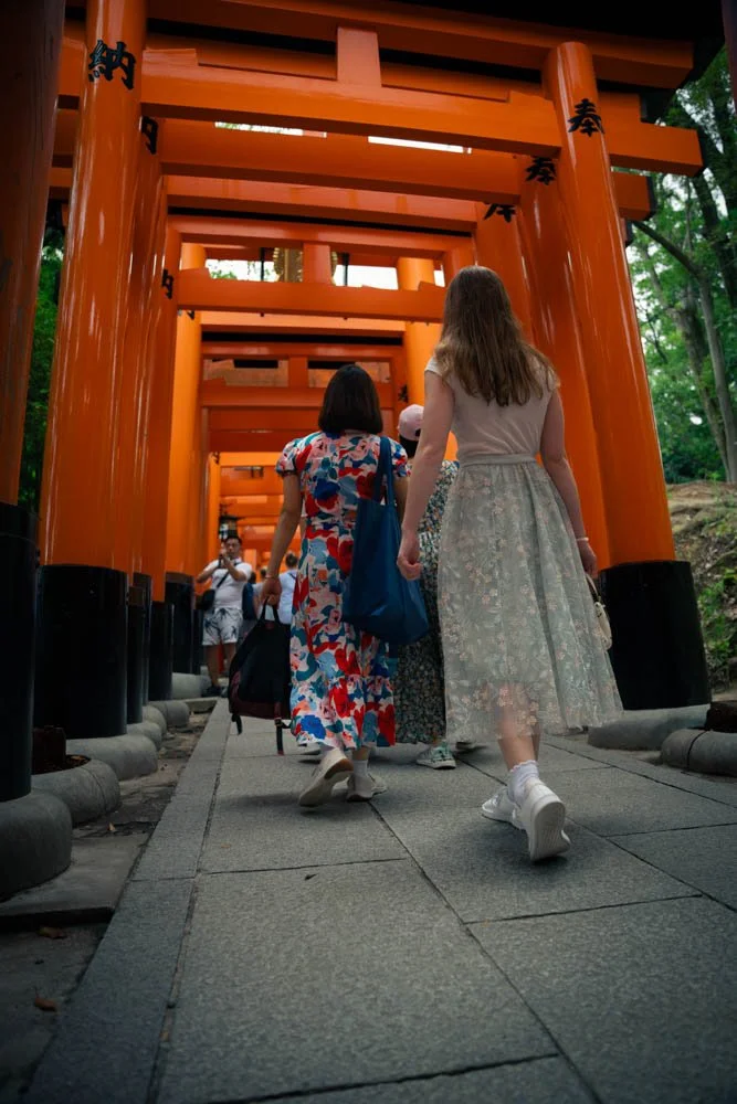 People walking through a path with multiple orange torii gates at a Japanese shrine or temple.