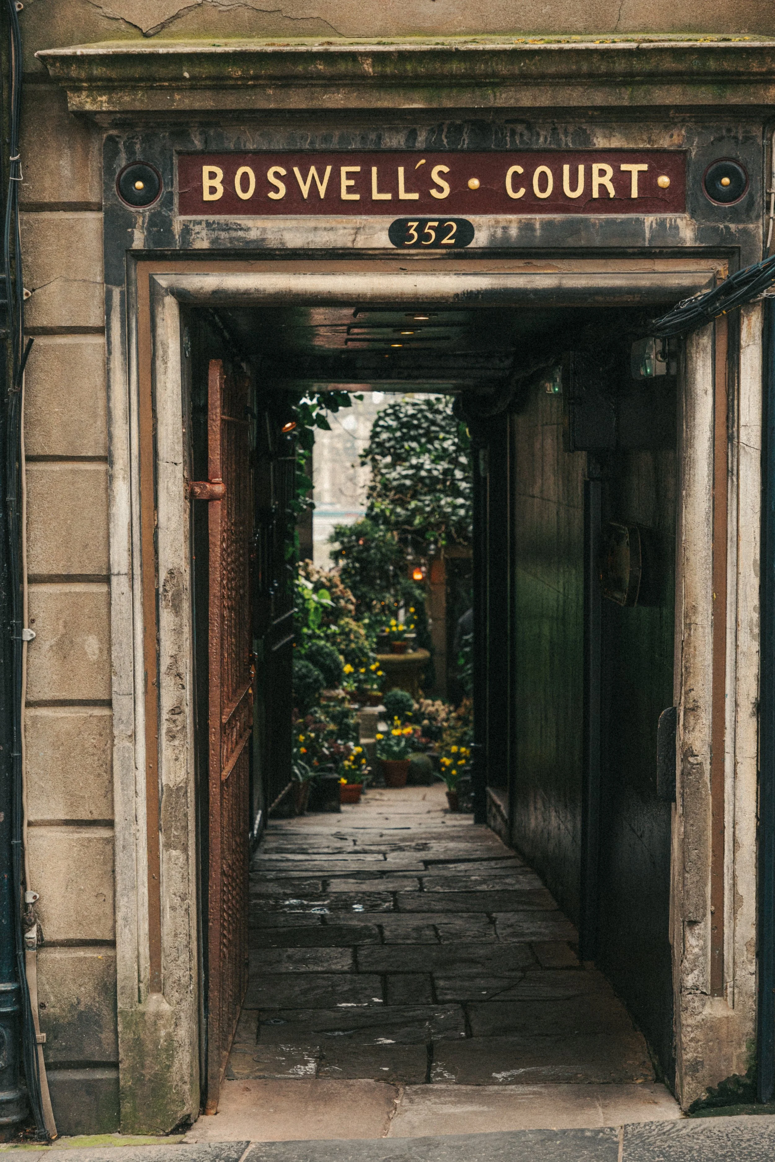 Entrance to Boswell's Court with a sign showing the address 352 and a view into a garden filled with potted plants and flowers.