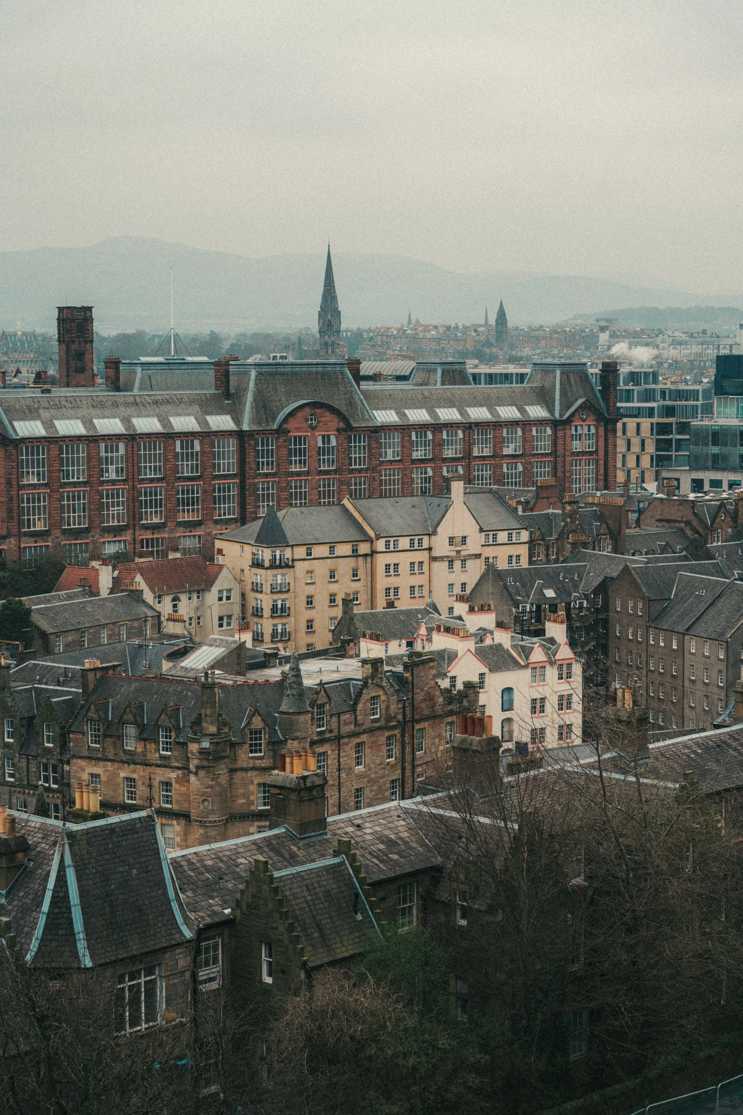 A cityscape featuring historic and modern buildings with a church steeple in the distance, under a cloudy sky.