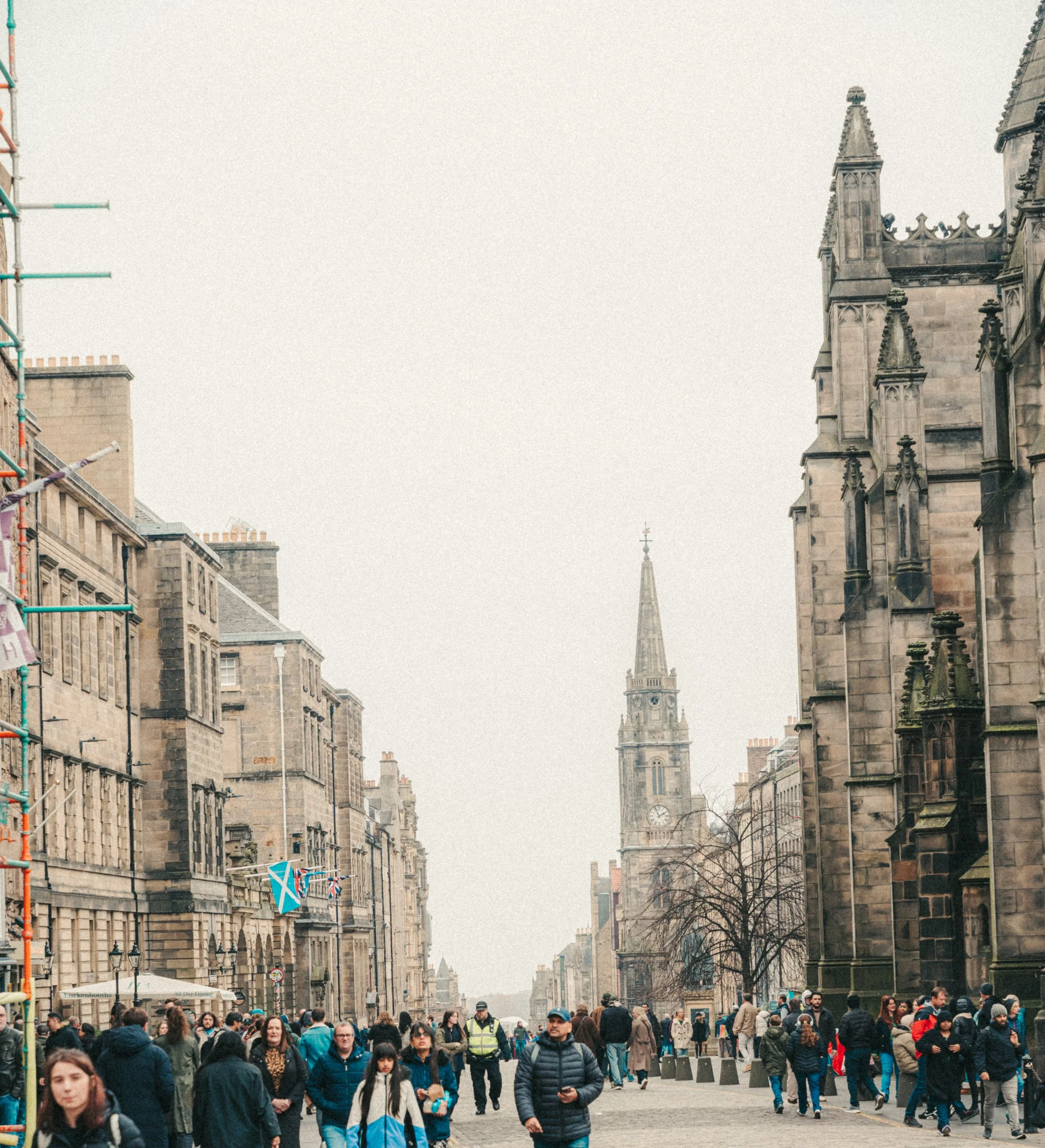 Bustling city street filled with pedestrians, historic buildings, and the church spire of the Abbey Church of Saint Mary on the background, in Oxford, UK.