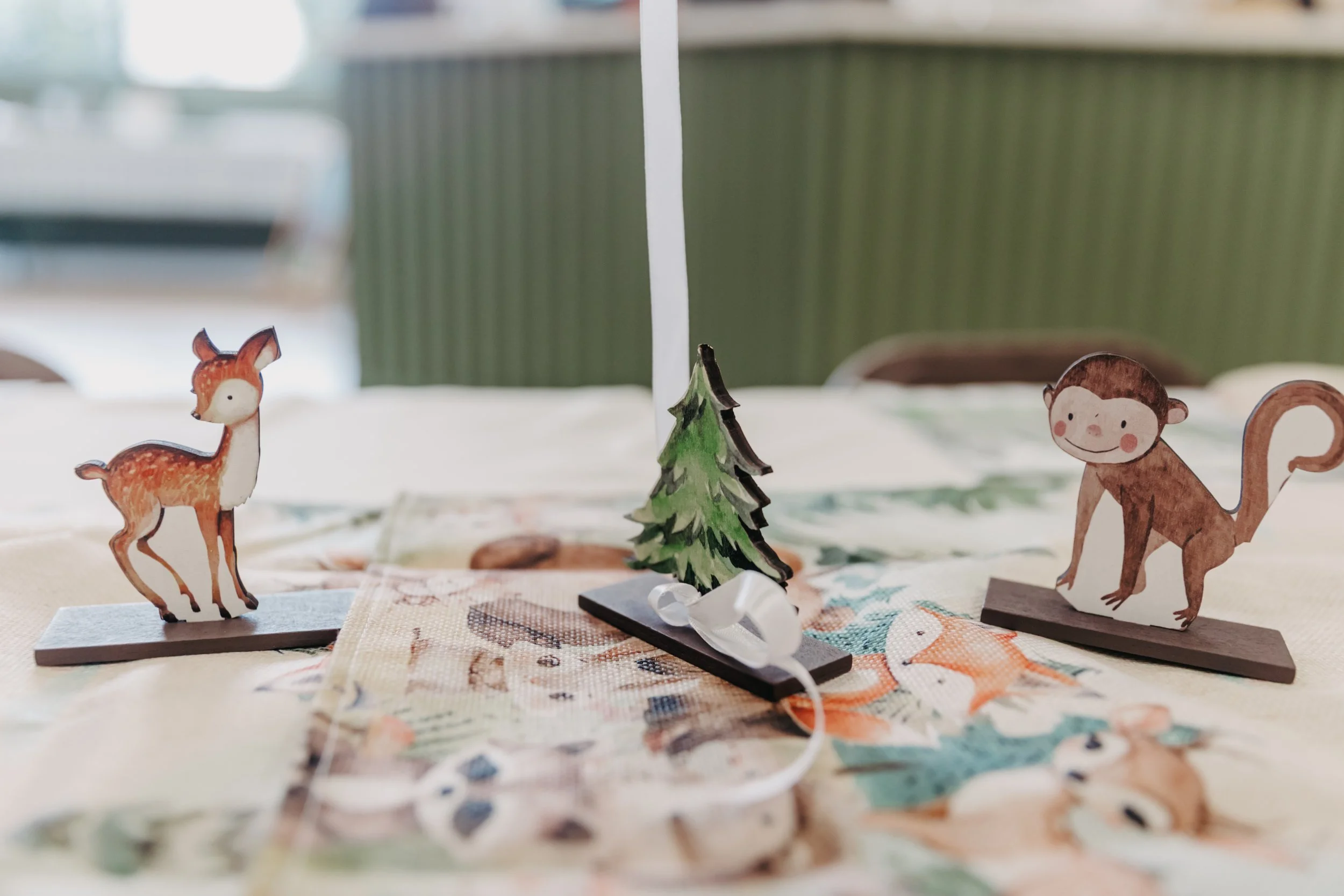 Decorative paper cutouts of a deer, a tree, and a monkey on display tables with a blurred background.