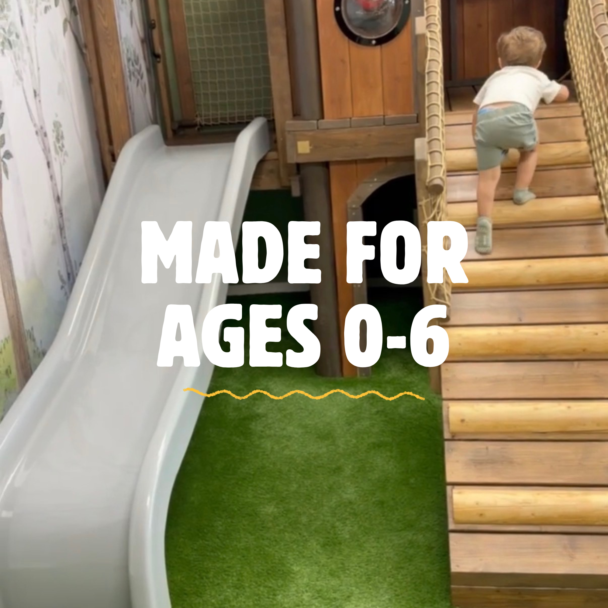 Little boy crawling on a wooden play structure with a slide and netting, in a play area with artificial grass.