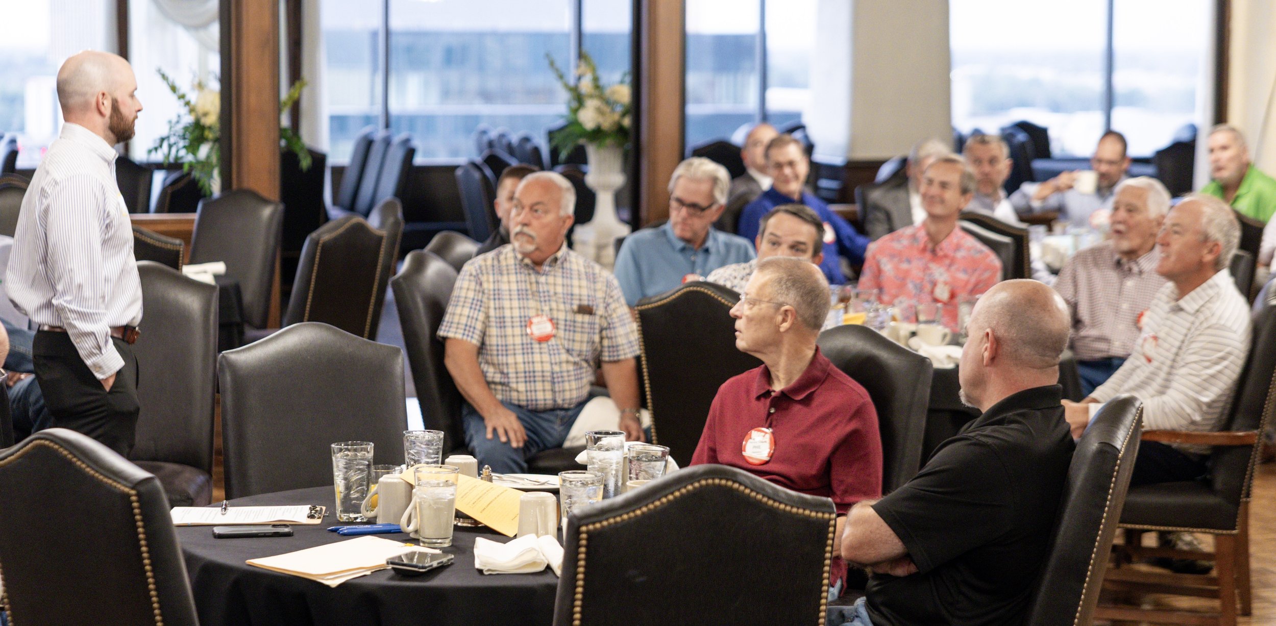 A member stands to speak during a Wichita Executives’ Association breakfast meeting while other members listen at nearby tables.