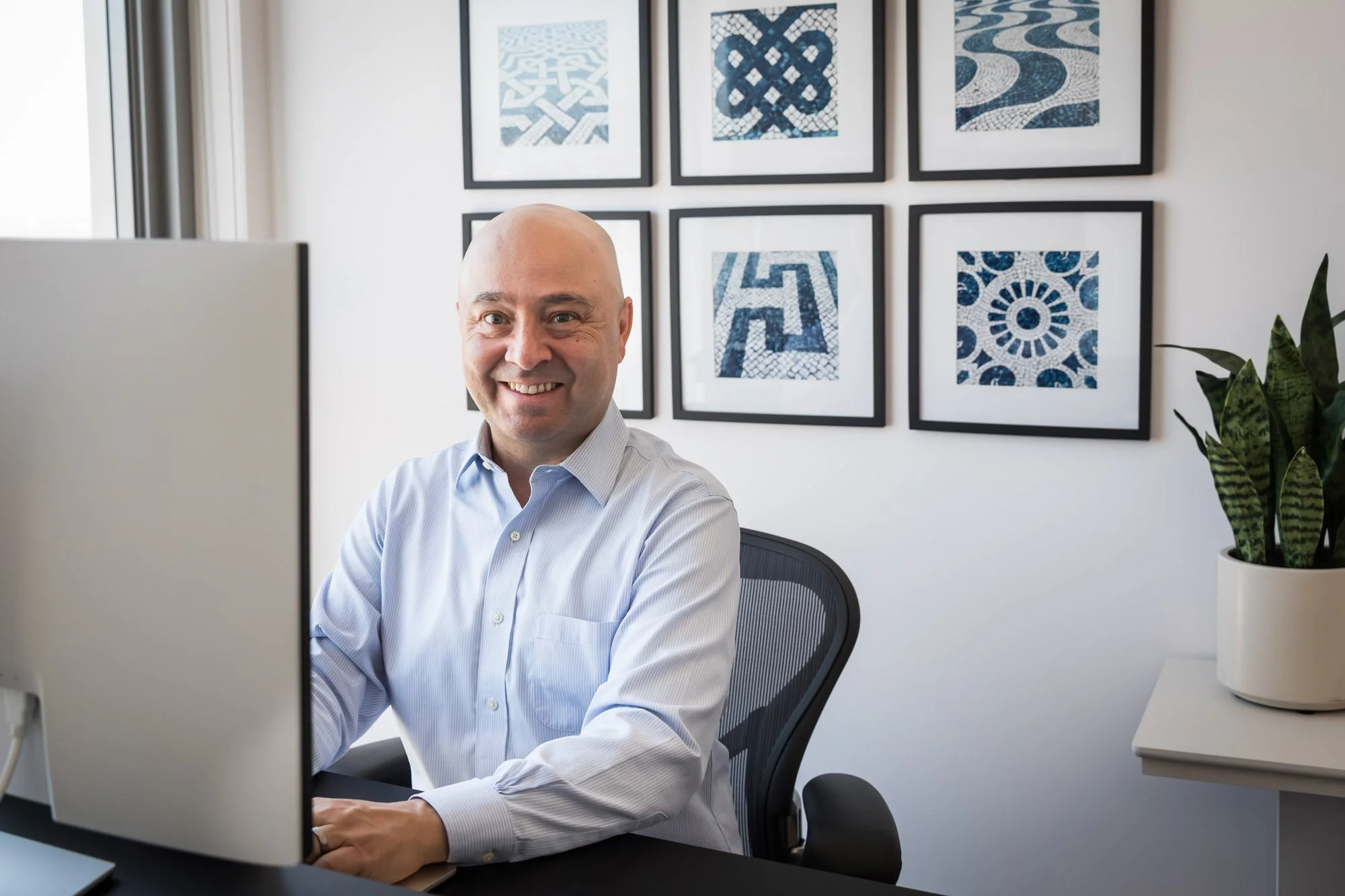 Career coach, Chris Lake, in a light blue dress shirt sitting at a desk in front of a computer monitor in an office.