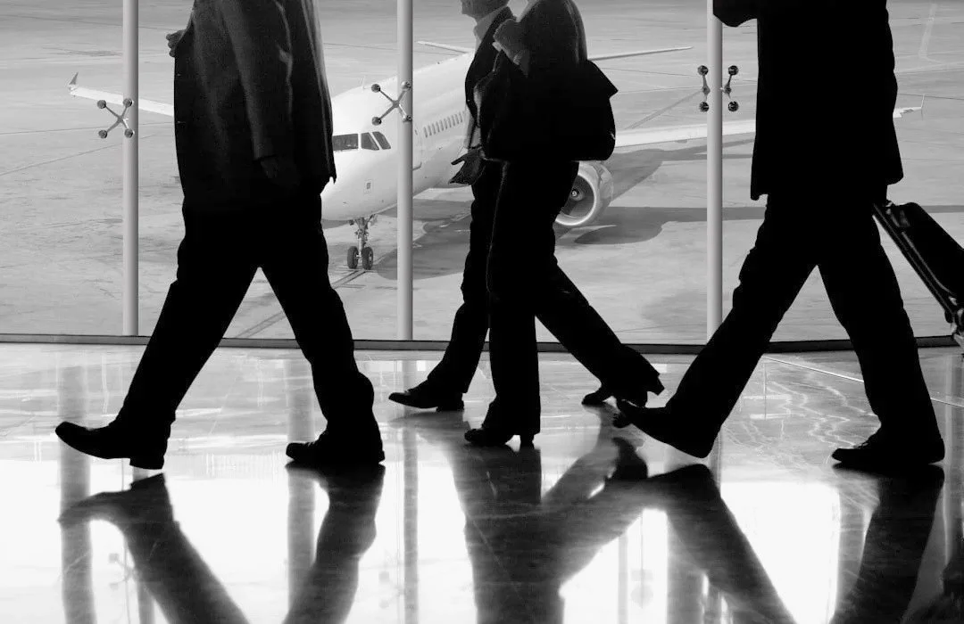Silhouettes of three business travelers walking through an airport terminal with a plane visible outside the window.