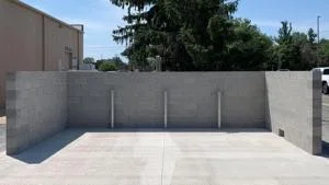 Empty parking space with a concrete wall on three sides, in an outdoor lot under a blue sky.