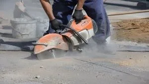 Worker using a concrete saw to cut through pavement at a construction site