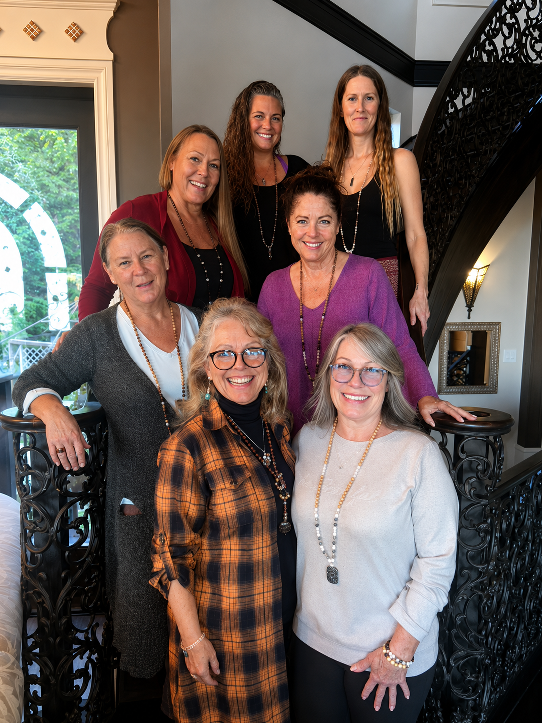 A group of nine women posing together indoors, smiling, standing on a staircase with a decorative black wrought iron railing.
