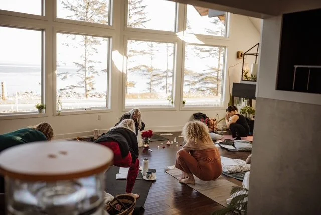 People participating in a yoga or meditation class in a bright, spacious room with large windows overlooking a snowy landscape.