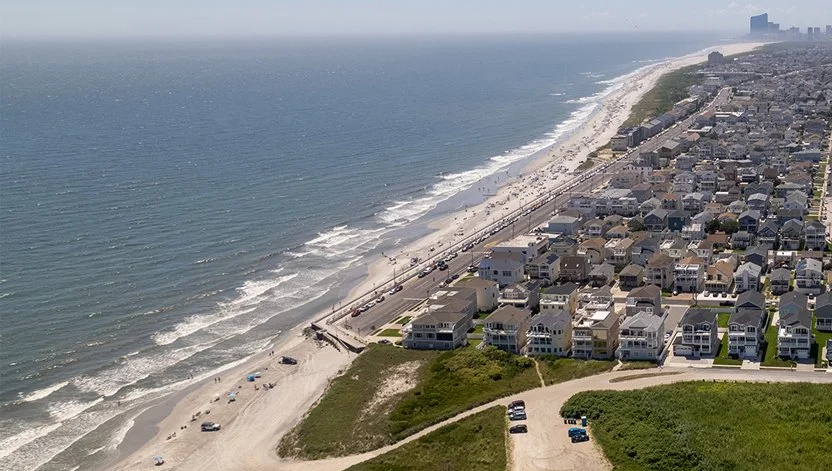 Aerial view of a beach town with houses along the shoreline, a beach with umbrellas, and the ocean extending into the horizon.