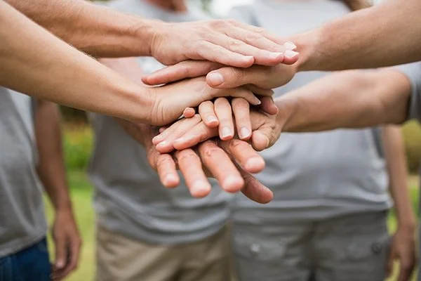 A group of people with hands stacked together in a gesture of teamwork or unity outdoors.