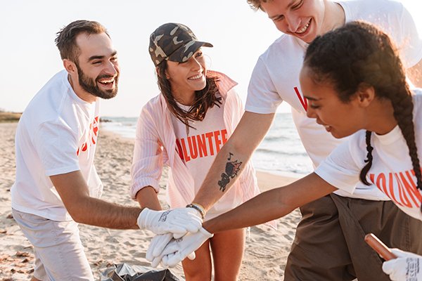 Group of four volunteers on a beach, smiling and holding hands in a teamwork gesture.