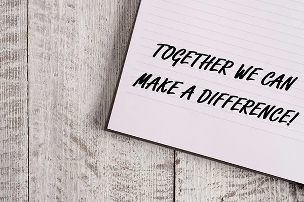 A white sheet of paper with a handwritten message that says "Together we can make a difference!" on a light wooden surface.