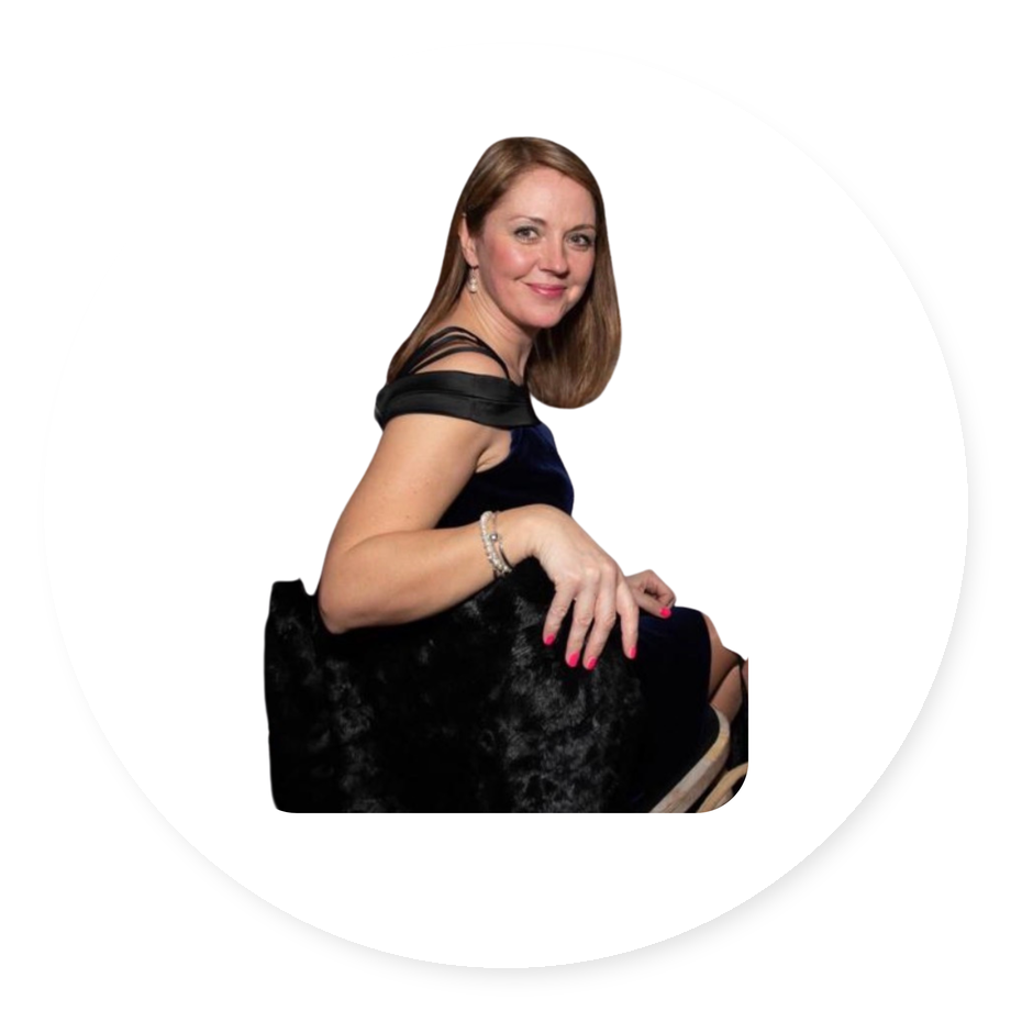 A woman with shoulder-length brown hair wearing a dark blue dress with black straps, sitting on a black furry chair, smiling at the camera.