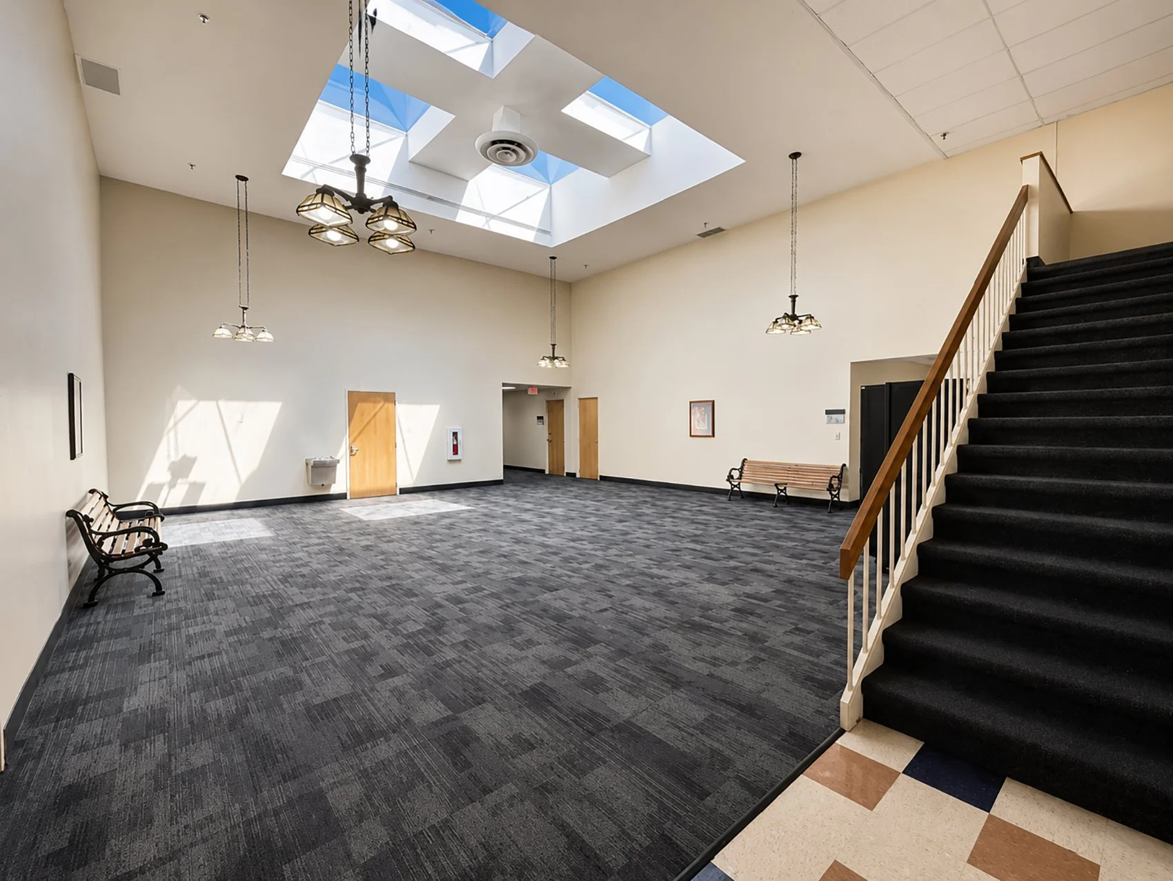 Indoor space with sunlight coming through large skylights, benches, and a staircase with black carpeted steps.