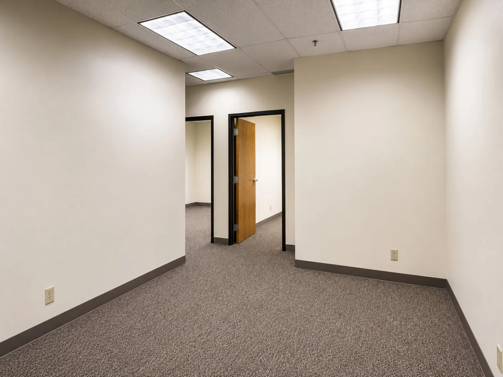 Office hallway with beige walls, gray carpet, and open doors.