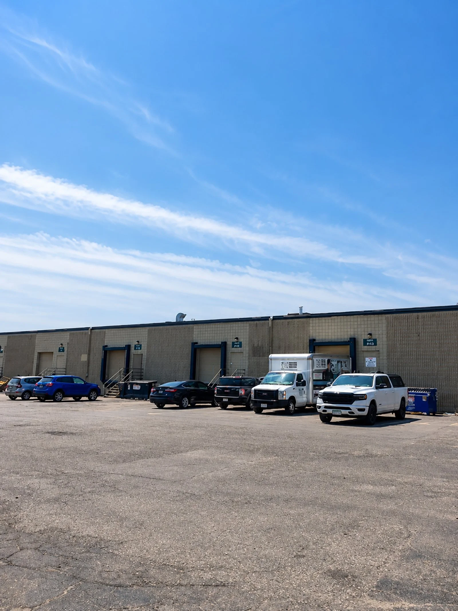 Parking lot with several parked cars and a building, under a blue sky with some clouds.