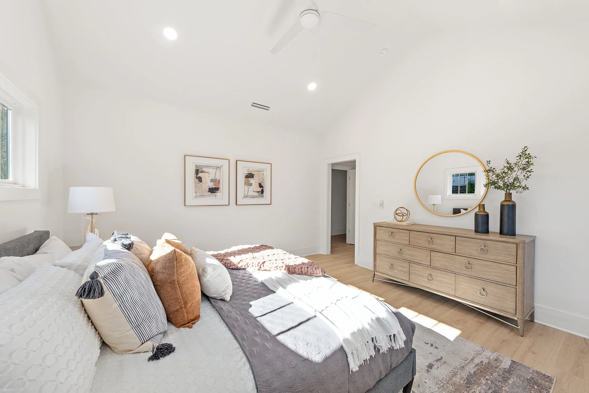 Staged bedroom with round mirror and wood dresser