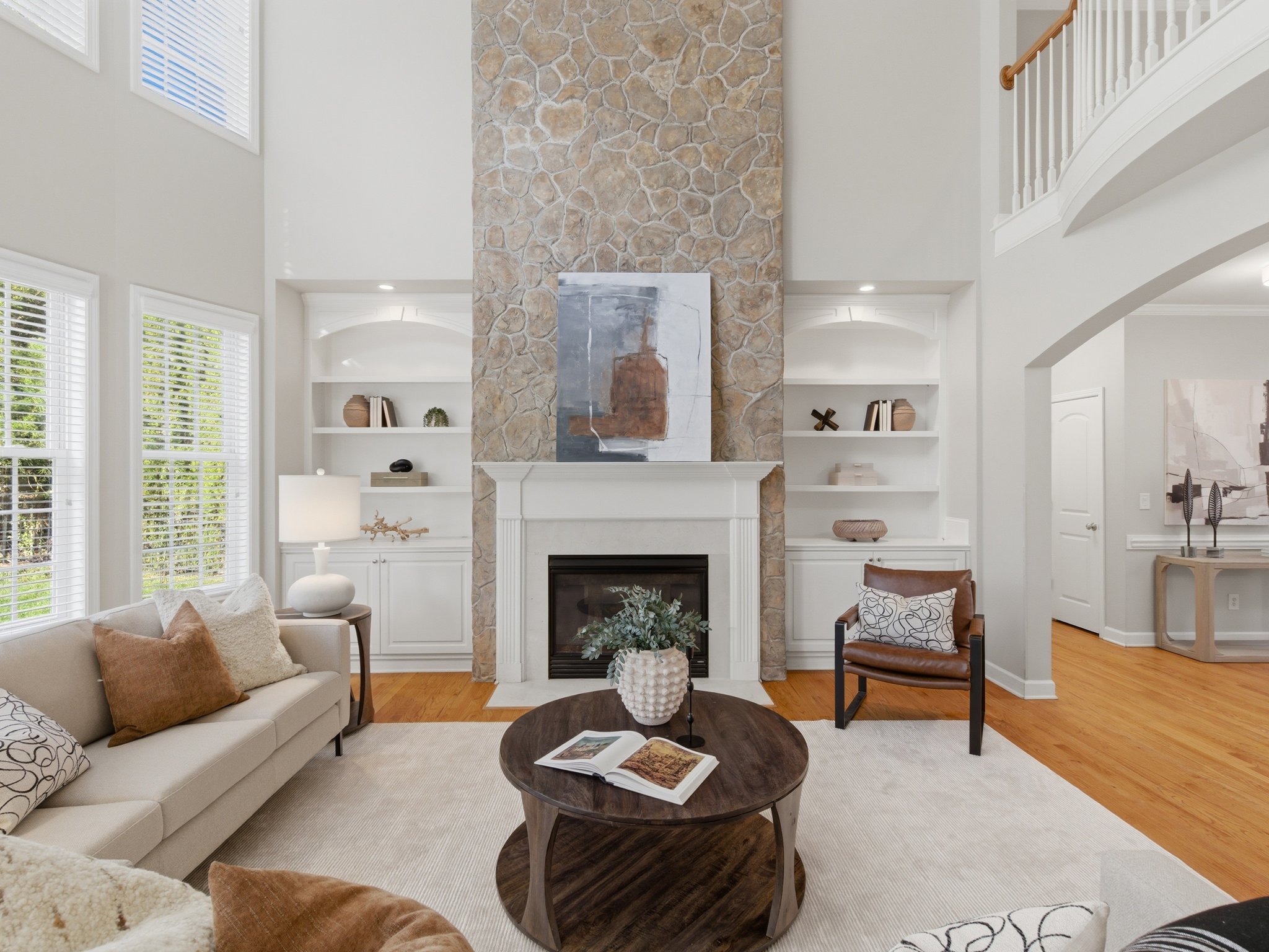 Staged living room with tall stone fireplace and built-in shelving