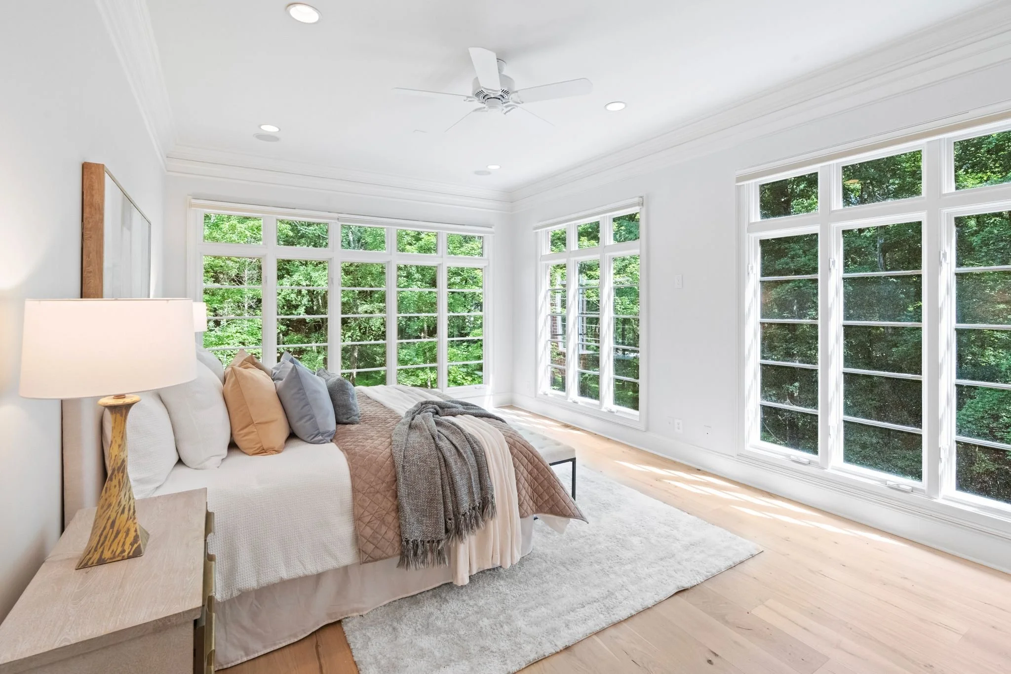 Staged primary bedroom with wall of windows and warm bedding