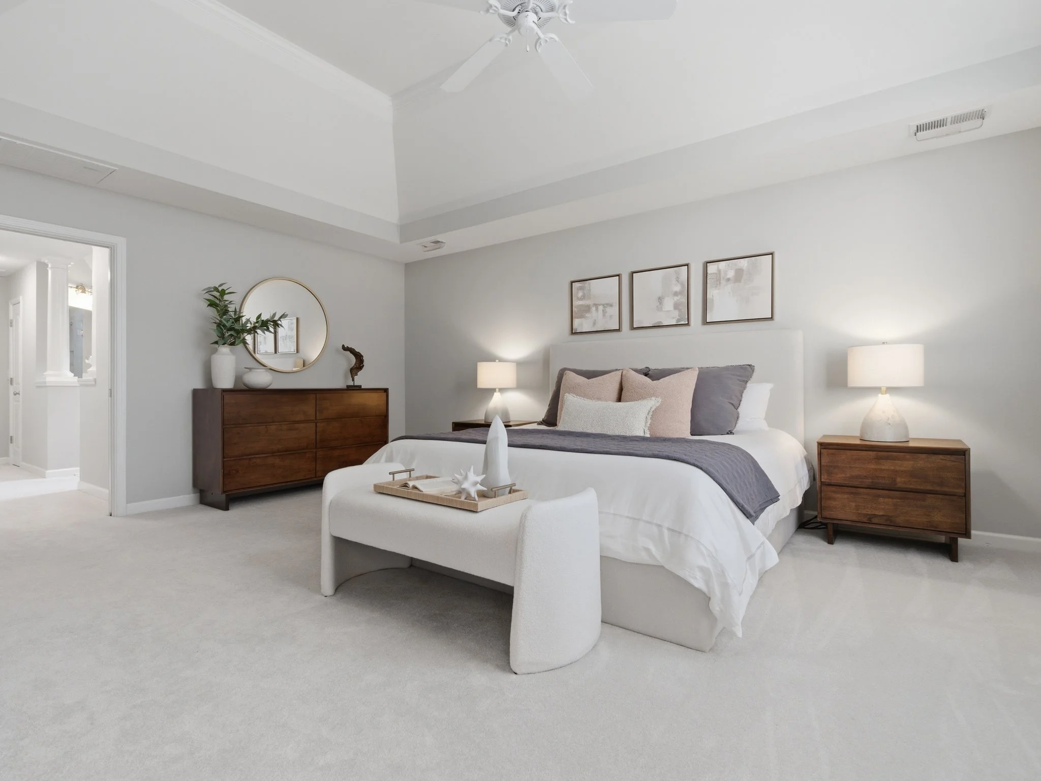 Staged primary bedroom with round mirror and wood dresser