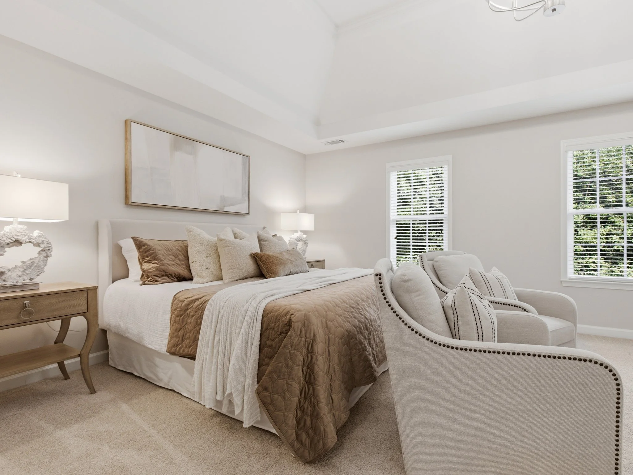 Staged primary bedroom with camelback chair and warm bedding