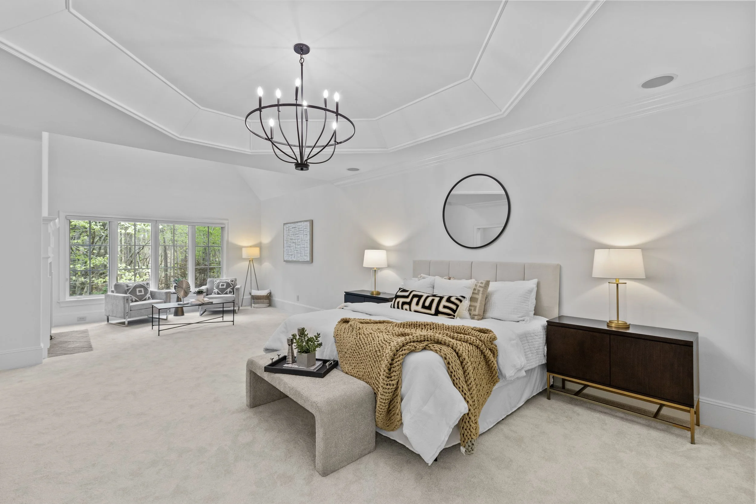 Staged primary bedroom with sitting area and tray ceiling