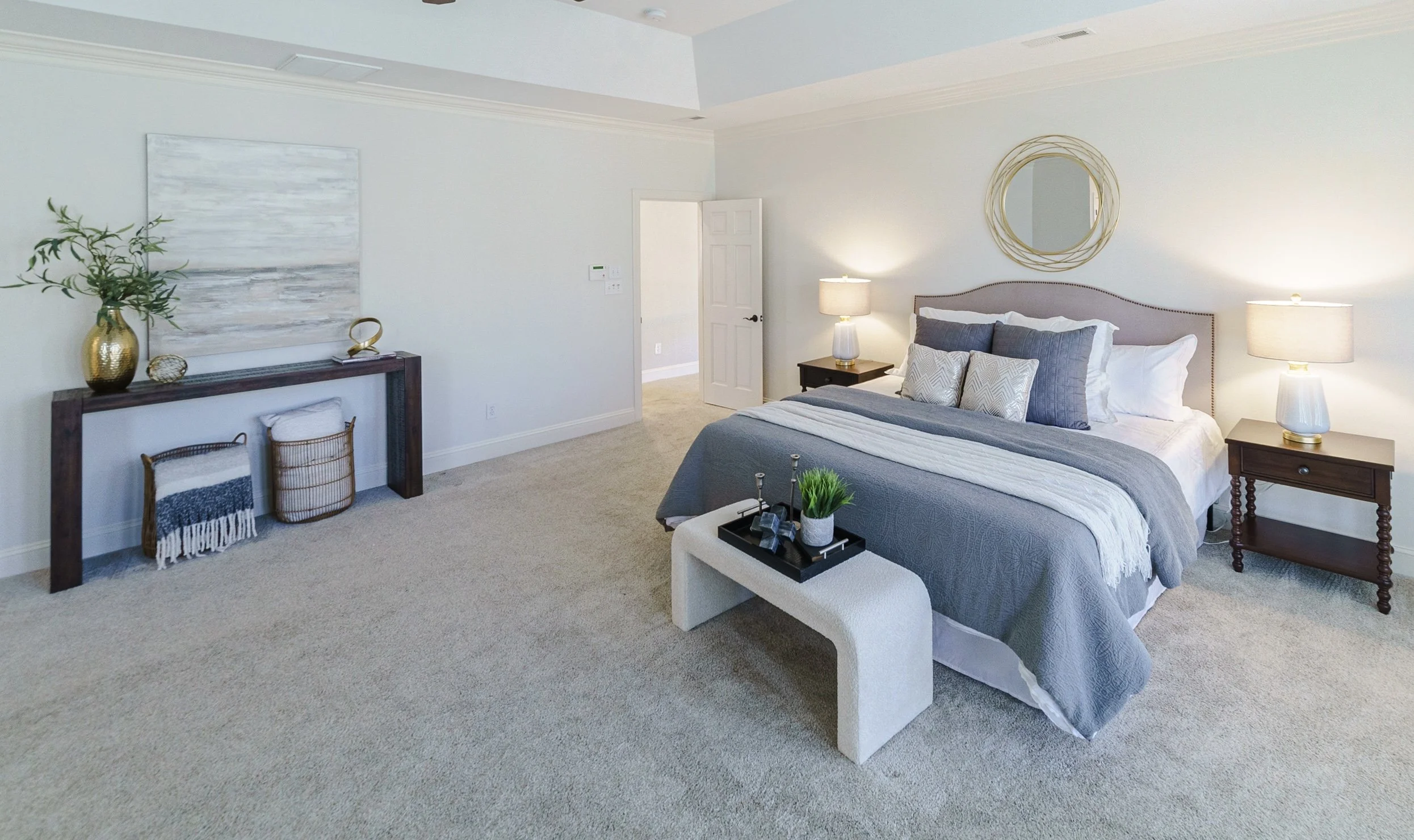 Staged primary bedroom with round mirror and console table