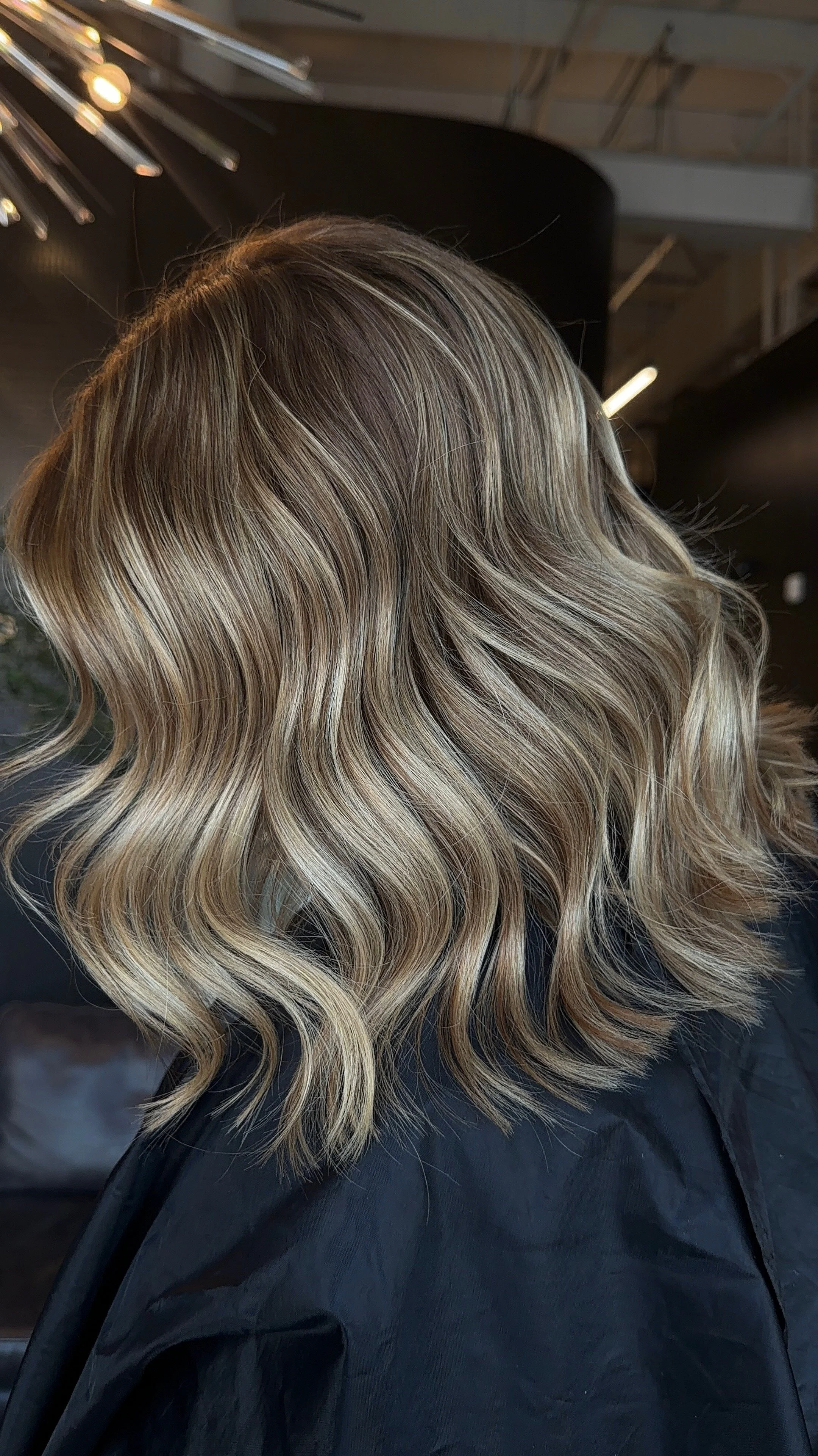 Close-up of blonde hair styled in loose waves, with a mix of darker roots and lighter highlights, in a salon setting.
