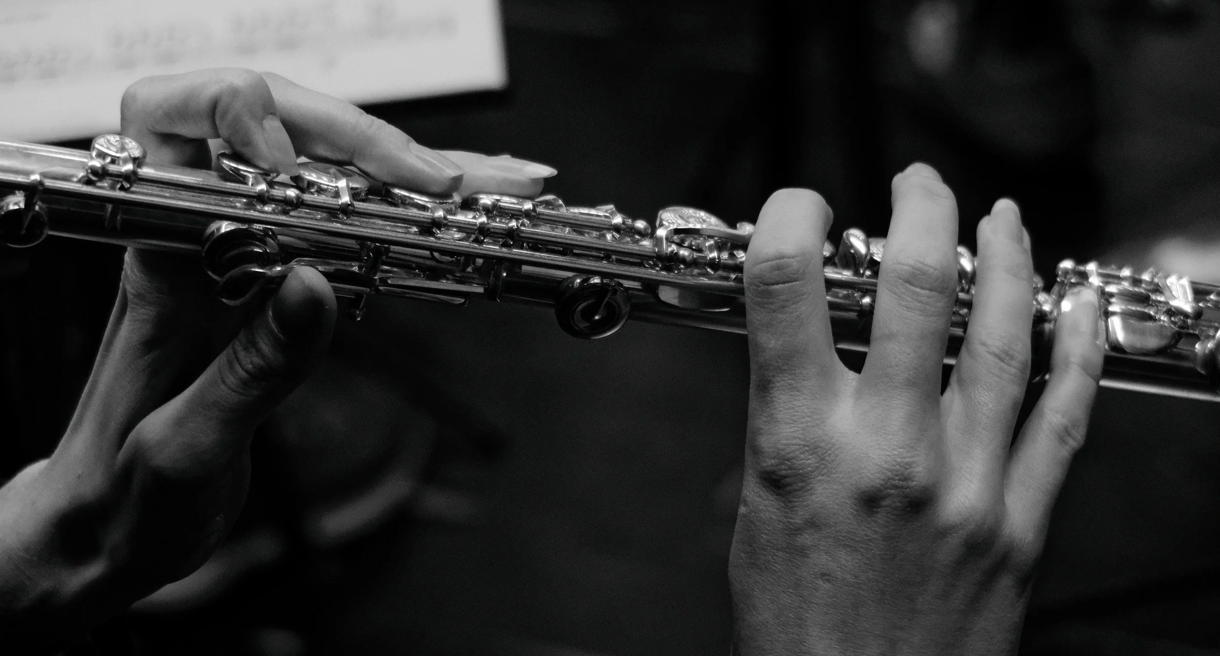 Close-up of a person’s hands playing a silver flute in black and white.