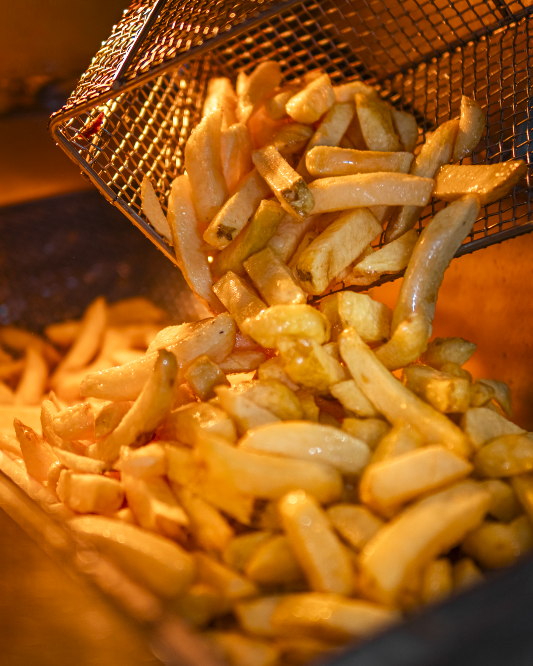 A metal basket filled with freshly fried French fries being poured into a container.