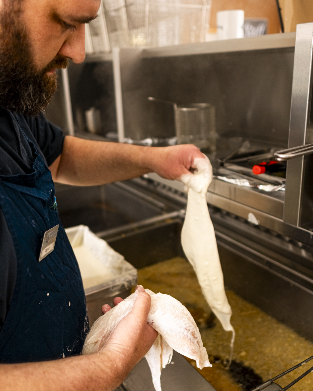 Man frying food with batter in a commercial kitchen.