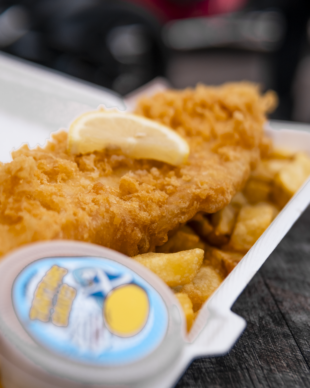 Fried fish fillet with lemon wedge and French fries in a white takeout tray.