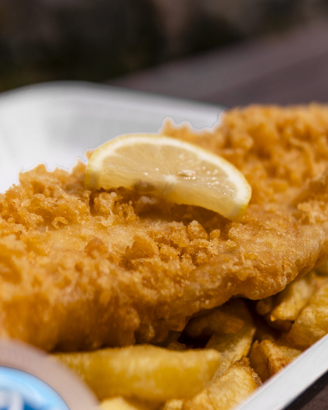 Close-up of a piece of fried fish with a lemon wedge on top, served with French fries.