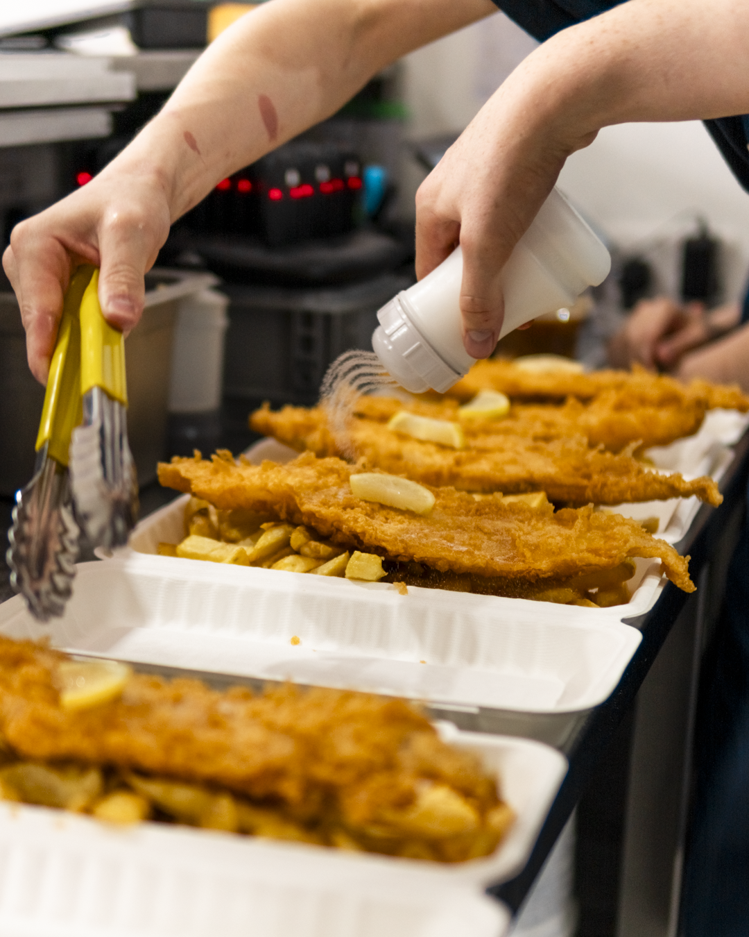 Someone seasoning fried fish fillets with lemon slices in a styrofoam food container.