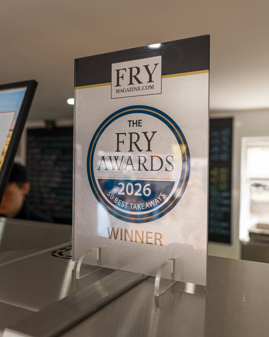 A sign on a counter indicating the Fry Awards 2026, winners of the 50 best takeaways, from Fry Magazine.