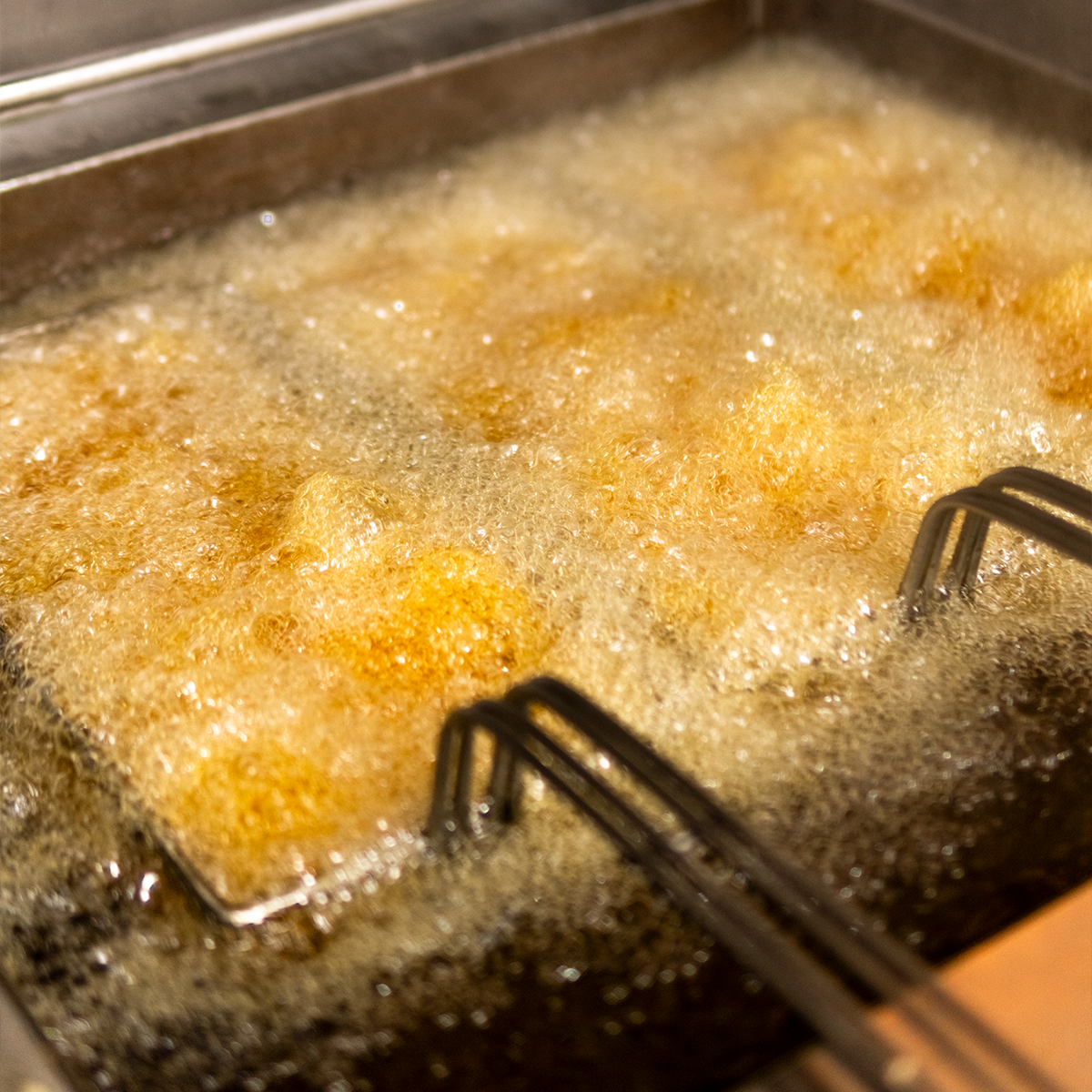 Frying food in hot oil in a deep fryer or skillet, with bubbles forming on the surface.