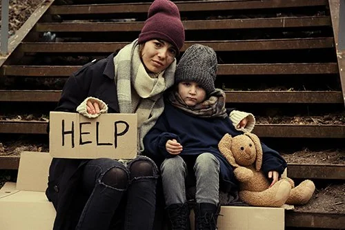 Woman and child sitting on outdoor stairs, holding a cardboard sign that says Help, with a teddy bear.