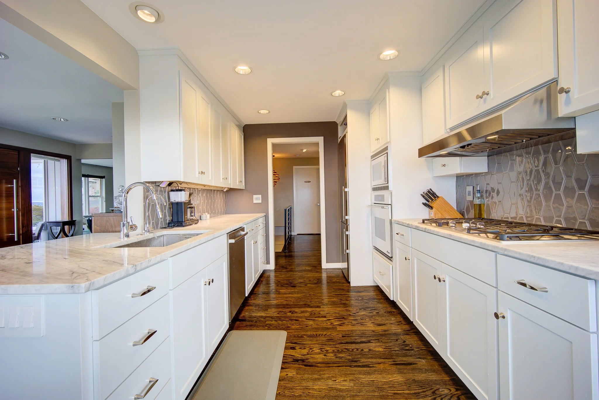 Modern kitchen with white cabinets, marble countertops, a gas stove, and a dark hardwood floor.