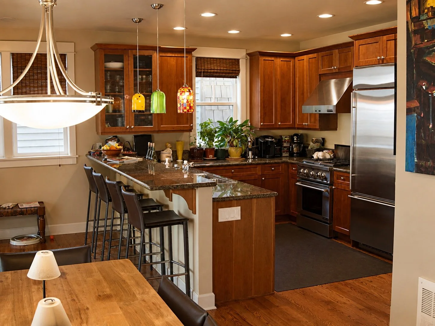 Kitchen with wooden cabinets, black granite countertops, stainless steel appliances, three colorful pendant lights, and a plant on the counter.