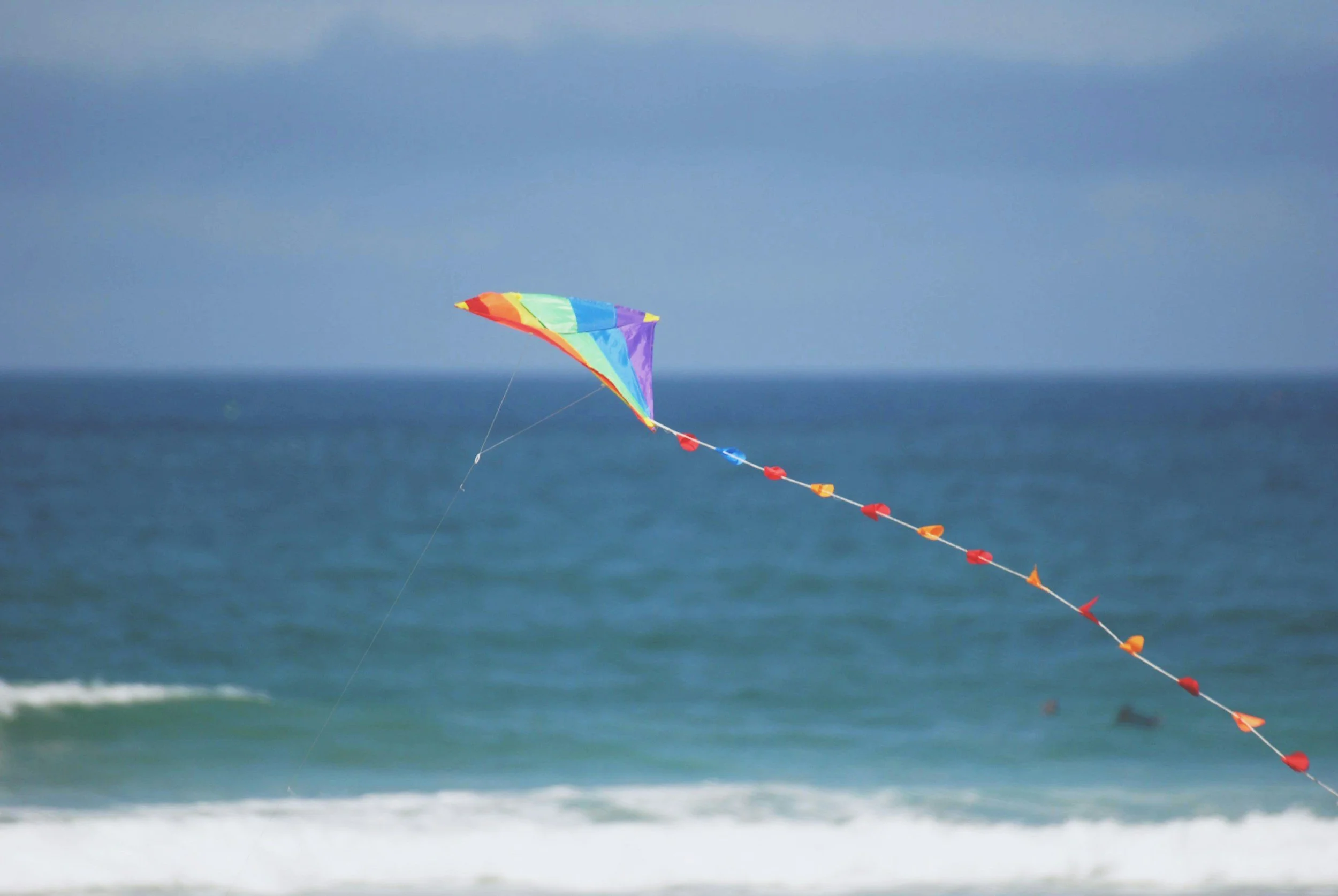 Colorful kite flying over the ocean on a cloudy day.