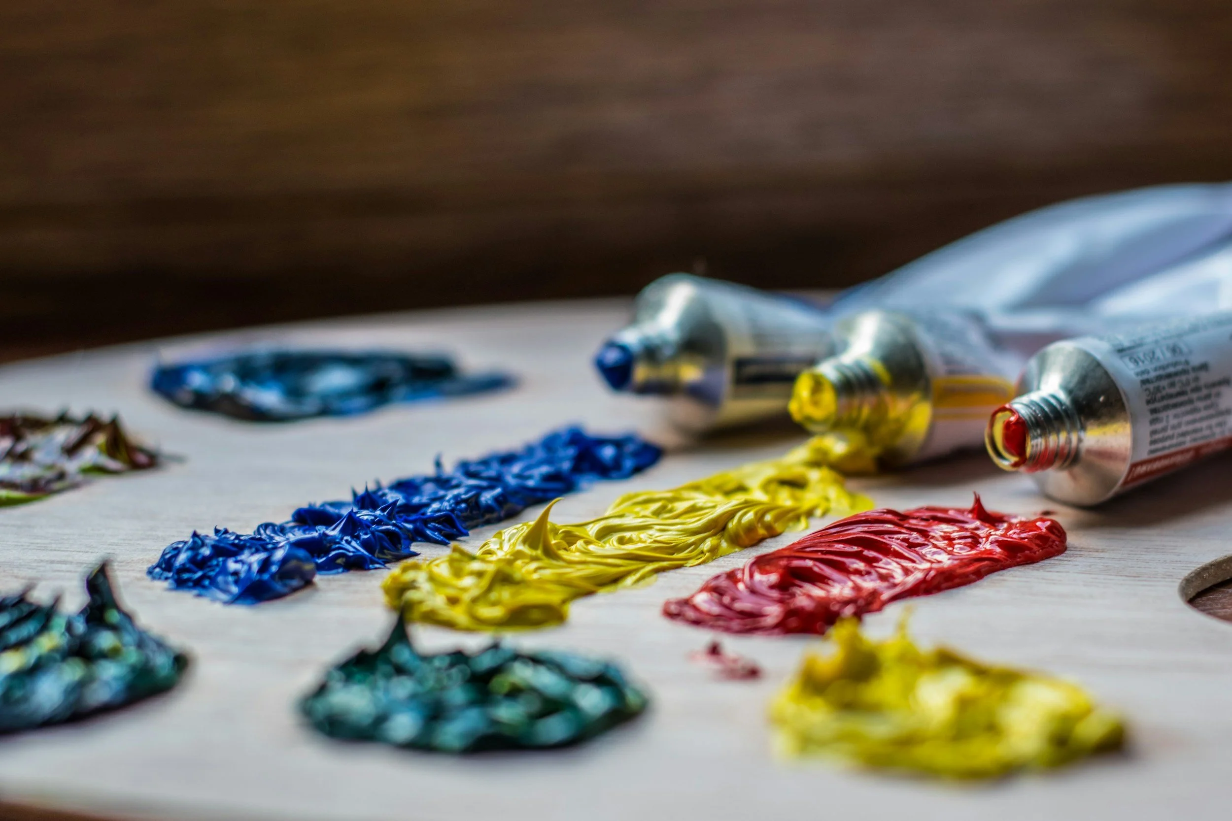 Assorted colors of paint squeezed out in thick lines on a flat surface with paint tubes in the background.